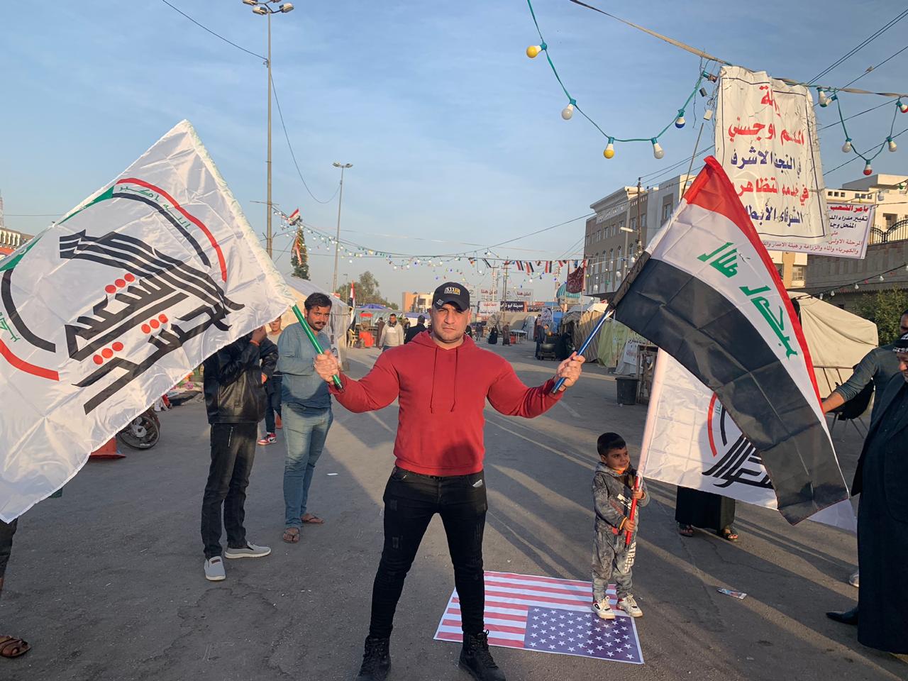 بالصور : متظاهرون يحرقون العلم الامريكي وسط ساحة الصدرين في النجف ويرفعون علم العراق والحشد الشعبي
